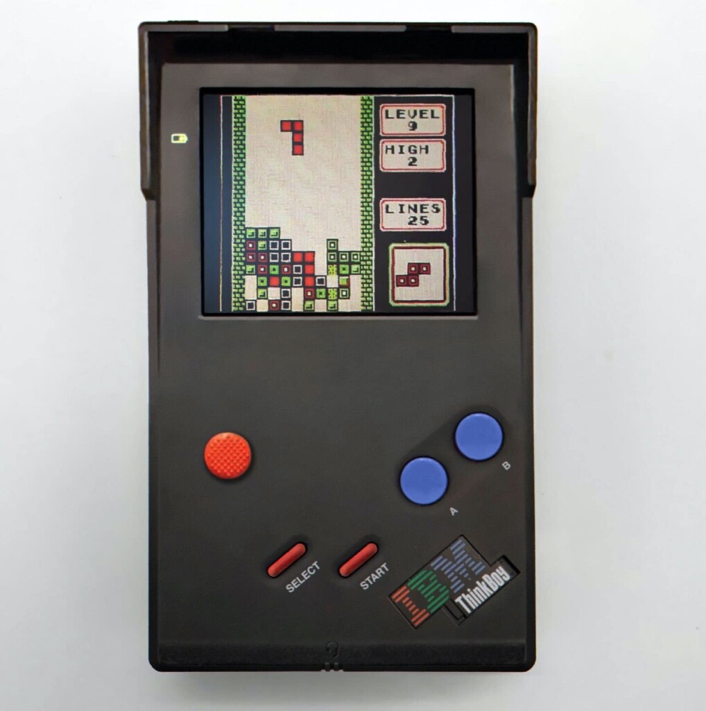 A picture of an electronic gaming device with IBM ThinkPad styling, but ever so slightly reorganised Nintendo GameBoy layout. There are A and B buttons, Select and Start, a screen shade, and instead of a direction pad, a beautiful simple red TrackPoint.